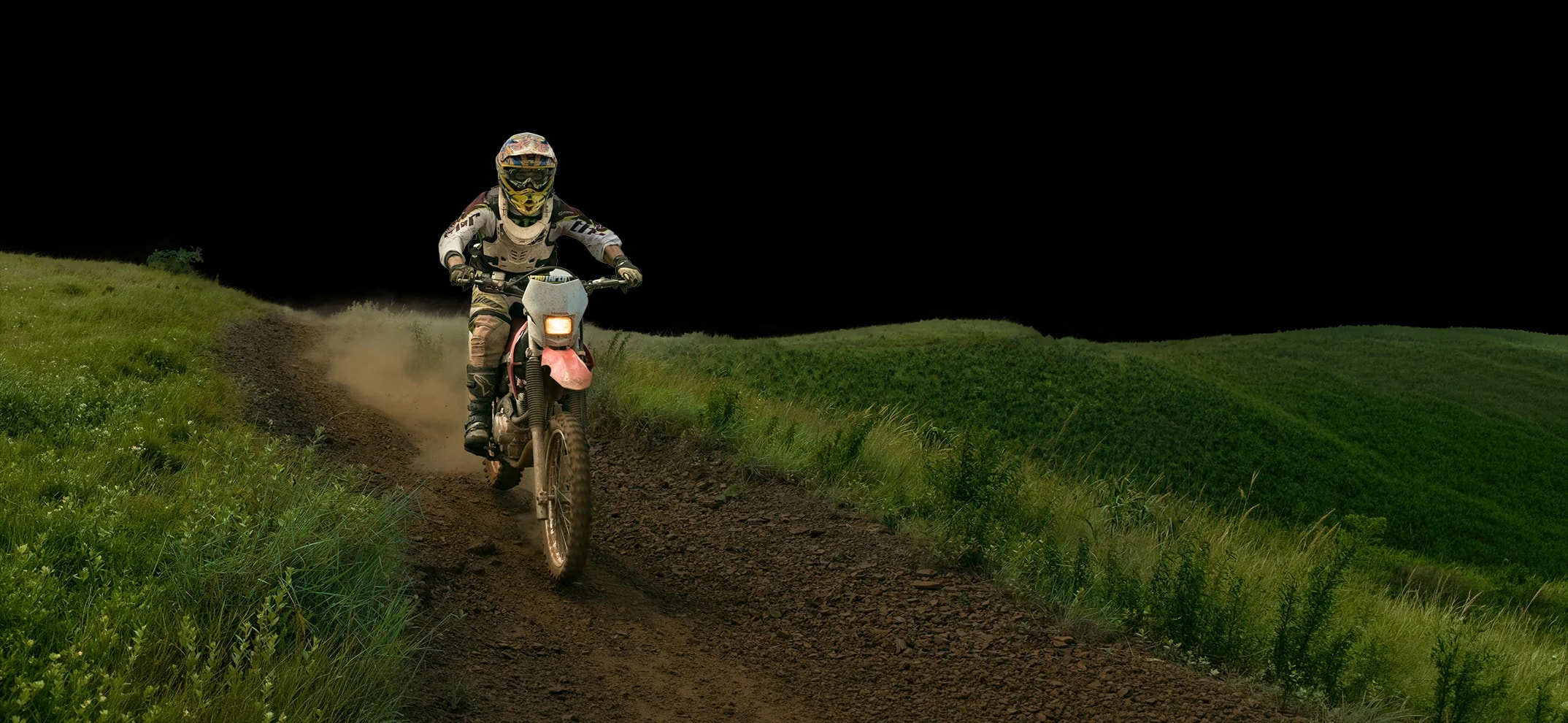 Enduro rider on a dirt trail through rolling green hills